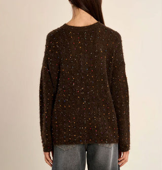 Model with back to camera wears a slouchy brown sweater with multicolored fabric flecks and small sequins sewn in