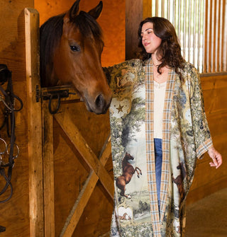 Model standing in front of a horse's stall wears a long, kimono-style robe with horse motif and contrasting plaid borders