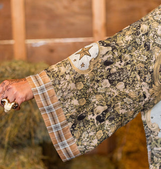 Model's extended arm shows the floral details of a garment sleeve with contrasting plaid border and star accents inside a gold frame