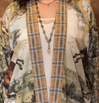 Model wears a horse-themed open-front tunic with floral and landscape designs and an orange plaid border