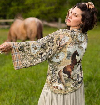 Model standing in a horse pasture with one arm outstretched wears a horse-patterned tunic with long, wide sleeves and, plaid cuff and star accents