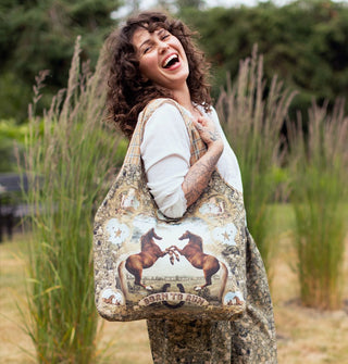Model smiling broadly wears a tote bag over shoulder that features an image of two rearing horses above a banner that reads, "Born to run"