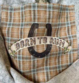 Plaid interior tote bag pocket features a banner that reads, "Born to run" in front of a horseshoe graphic