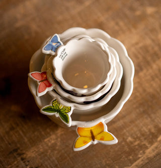 Set of four white ceramic measuring cups stacked one inside of the other feature colorful butterfly handles