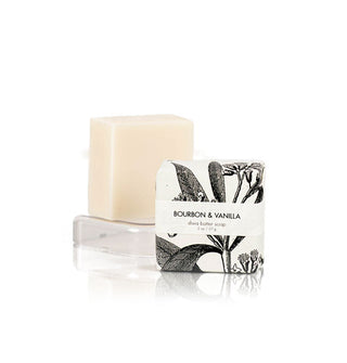 Two 2-ounce bars of Bourbon & Vanilla Shea Butter Soap, one wrapped in black and white botanical print paper and the other unwrapped on a clear rectangular pedestal