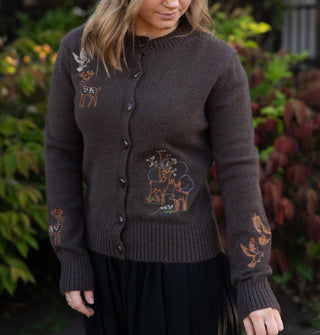 Model wears a brown long-sleeved button-down cardigan with colorful deer, bird, and plant embroidery on its bodice and sleeves