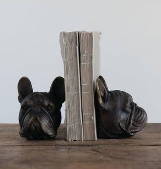 Pair of antiqued bronze bulldog head bookends, one forward-facing and the other in profile view, support two spineless, case-bound books on a wooden surface