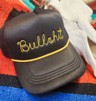 Black trucker-style hat with mesh back and gold rope accent says, "Bullshit" in embroidered script