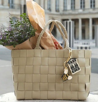 Bumblebee and house keychains hang from the strap of a woven tote holding a bouquet of flowers