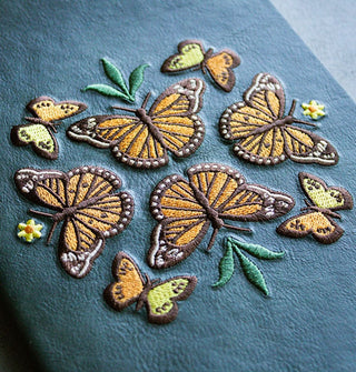 Detail of monarch butterfly embroidery on a green suede-like journal hardcover