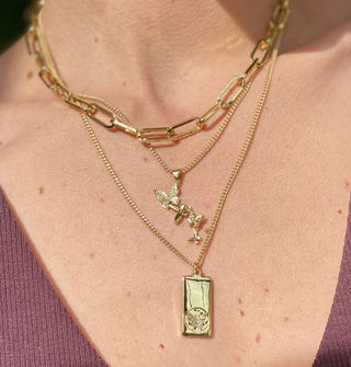 Model wears three gold necklaces, two with pendants and one large-link chain