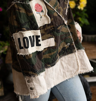 Model wears a camouflage print and white patchwork jacket with raw seams and "Love" patches on the chest and sleeve