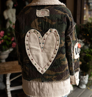 Model facing away from the camera wears a camouflage print and white patchwork jacket with raw seams and a large white heart patch with stud accents on the back