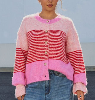 Model wears a button-down cardigan with gathered, voluminous sleeves and bands of light and bubblegum pink separated by a central section of dense red horizontal stripes