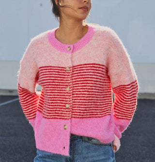 Model wears a button-down cardigan with voluminous sleeves and bands of light and bubblegum pink separated by a central section of dense red horizontal stripes