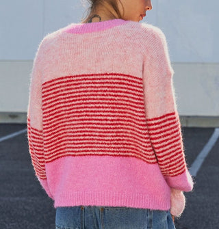 Model facing away from the camera wears a button-down cardigan with gathered, voluminous sleeves and bands of light and bubblegum pink separated by a central section of dense red horizontal stripes