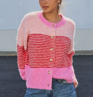 Model wears a button-down cardigan with bands of light and bubblegum pink separated by a central section of dense red horizontal stripes