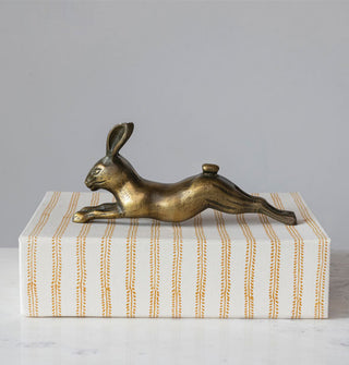 Brass-effect leaping rabbit sculpture atop a white and yellow fern-striped box