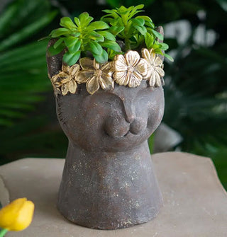 Gray stone cat bust planter with shiny gold flower crown detail holds a cluster of green succulents