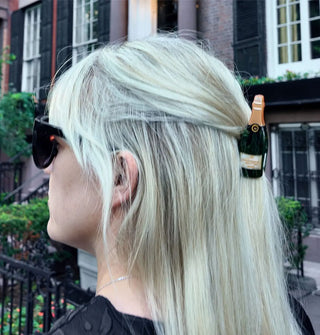 Model wears a champagne bottle claw clip in a partially swept-back hairstyle