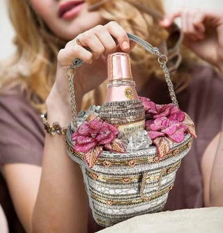 Model holds the strap of a beaded handbag designed to resemble an ice bucket with a bottle of champagne inside flanked by pink flowers