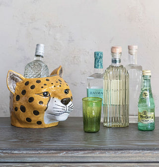 Ceramic cheetah head planter is staged as a bottle holder on a tabletop with other bottles and glassware