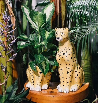 Ceramic sitting cheetah planter and ceramic sitting cheetah vase on a wooden pedestal among tropical foliage