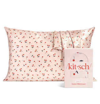 Light pink cherry print satin pillowcase is fitted on a standard size pillow with another case like it draped overtop and Kitsch box packaging placed in front