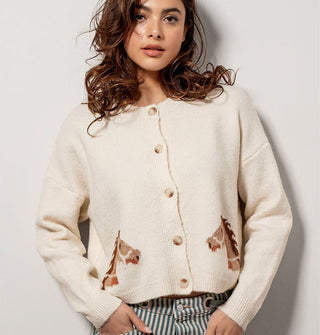Model wears a cream-colored cardigan with mirrored brown bridled horse designs near the bottom hem on either side of a 5-button placket