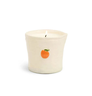 Cream-colored ceramic candle vessel with small orange fruit accent