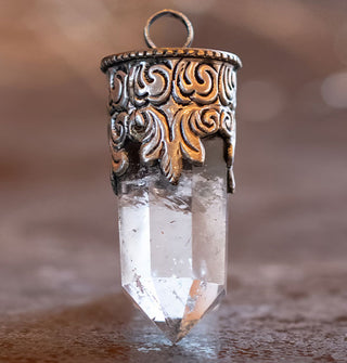 Polished clear crystal quartz point necklace pendant set in an ornately engraved silver setting with round bail at the top