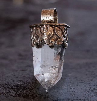 Clear crystal quartz point necklace pendant set in an ornately engraved silver setting with round bail at the top