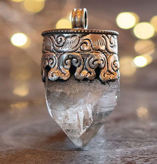 Clear crystal quartz point necklace pendant set in an ornately engraved silver setting with round bail at the top