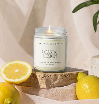 Lit Coastal Lemon candle rests on a stone slab flanked by lemons and linen