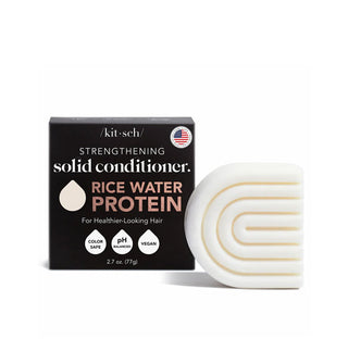 White ribbed C-shaped bar of Kitsch Rice Water Protein Strengthening Solid Conditioner is placed next to its black box packaging