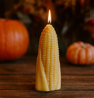 Lit beeswax corn cob candle on a wooden tabletop with pumpkins in the background