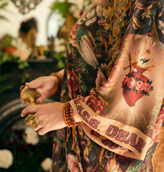 Model wears a silky robe with wide sleeve that features a sacred heart design accented by roses and the words, "Courage, dear heart" along the cuff