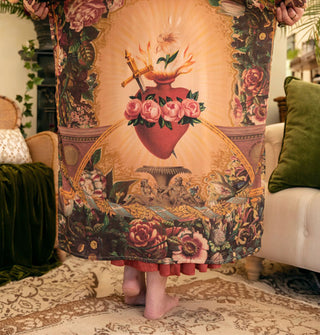 Model wears a long robe with sacred heart design flanked by lush florals