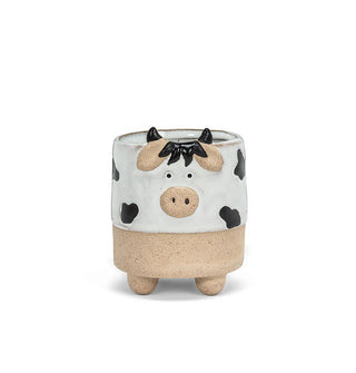 Cylindrical footed ceramic planter shaped and painted to resemble a cow with a matte brown base and black and white glossy body with whimsical facial features and horns