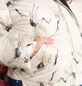Model's hand is slipped into the pocket of a white puffer jacket with flying cranes print