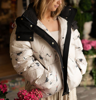 Model wears a hooded white puffer jacket with flying cranes print and black trim details