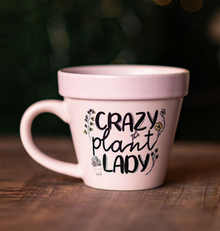 Pastel pink ceramic mug shaped to resemble a planter pot says, "Crazy plant lady" in alternating type styles accented with floral illustrations