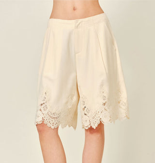 Model wears white wide-legged, knee-length shorts with lace hem detail