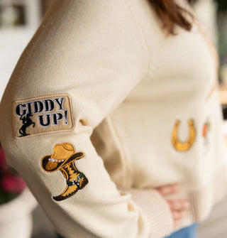 "Giddy Up!" bucking horse patch and cowgirl boot with pearl-accented Western hat on top patches on the sleeve of a cream-colored sweater