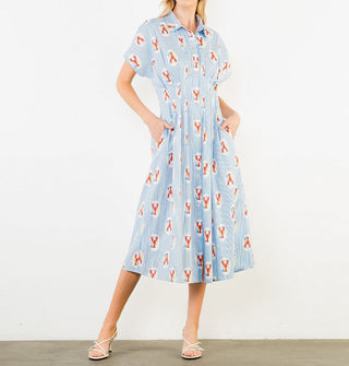 Model poses with hands in the pockets of a short-sleeved blue pinstripe midi shirt dress with collar and a print of lobsters in white ovals