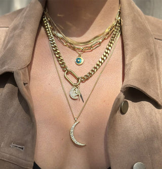 Model wears a collection of gold necklaces with varying chain and pendant sizes and styles