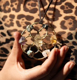 Model holds a gold Seed of Life pendant with seven crystals wired to it is strung on brown leather cord against leopard print fabric