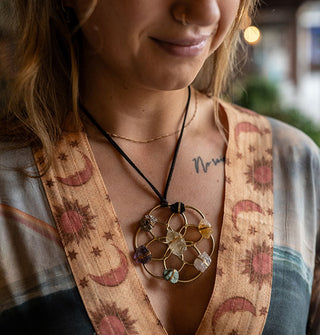 Smiling model in sun, moon, and star print robe wears a gold crystal grid pendant necklace