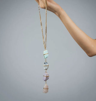 Model holds a necklace comprised of four rough-cut gemstones wrapped in gold wire on a gold curb chain
