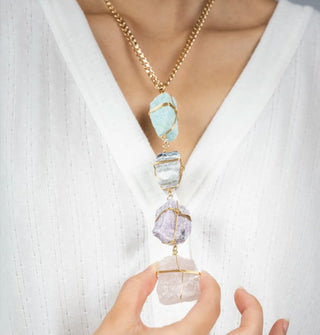 Model touches the bottom crystal on a necklace comprised of four rough-cut gemstones wrapped in gold wire on a gold curb chain